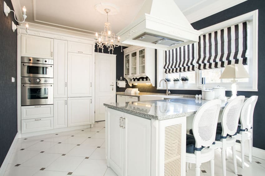 Kitchen with island, range hood, chandelier, countertop, white cabinets, roman shades, and chairs