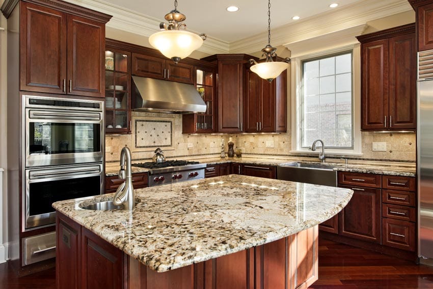 Kitchen with island, wood cabinets, cream granite countertops, backsplash, hanging lights, oven, and window