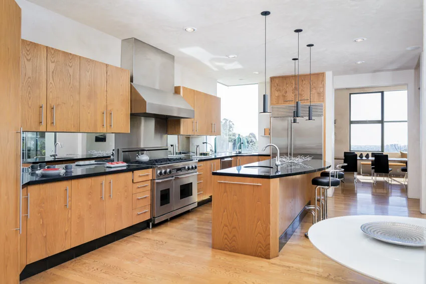 Kitchen with island, wood flooring, maple cabinets, pendant lights, range hood, and countertops