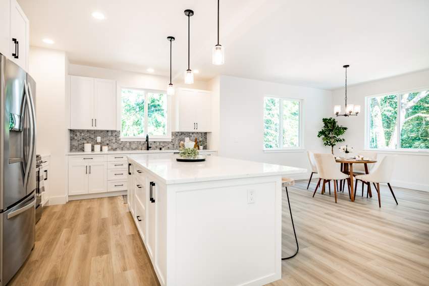 Kitchen with island, wood floors, countertops, cabinets, Mother of Pearl backsplash, table, chairs, and windows