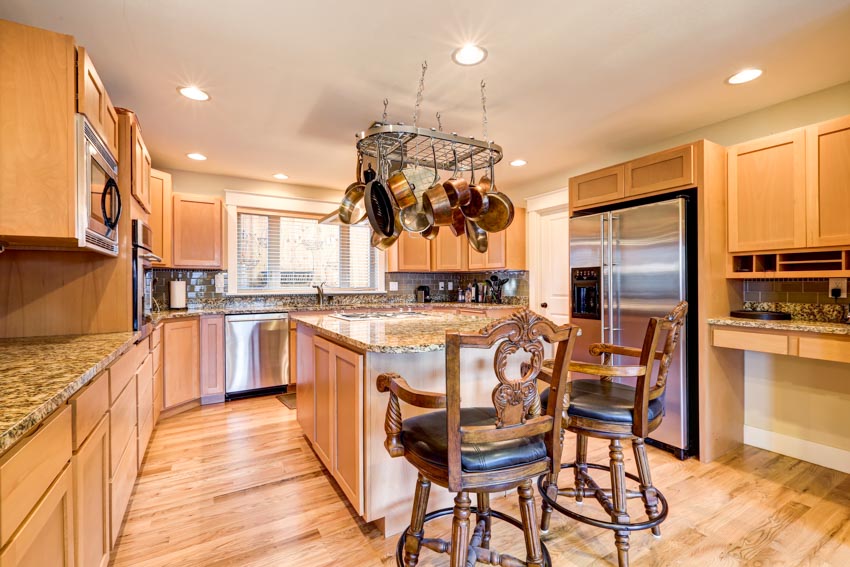 Kitchen with maple cabinets, island, chairs, wooden floors, hanging pot rack, countertop, and window