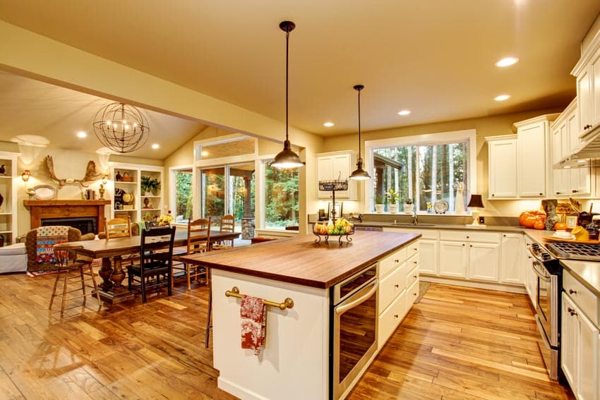Kitchen with microwave in island, countertops, cabinets, pendant lights, table, chairs, windows, and wood flooring
