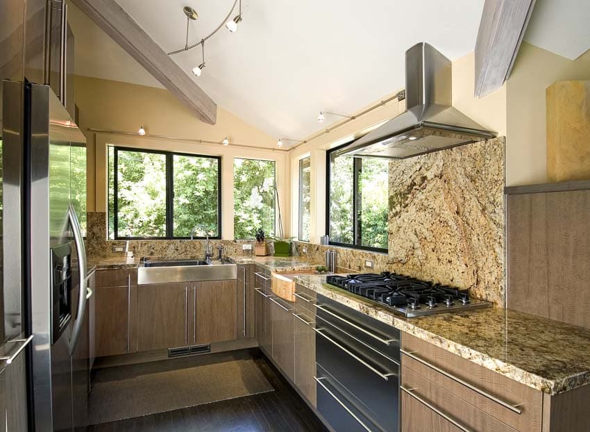 Kitchen with millennium cream granite countertop, backsplash, cabinets, stove, range hood, and windows