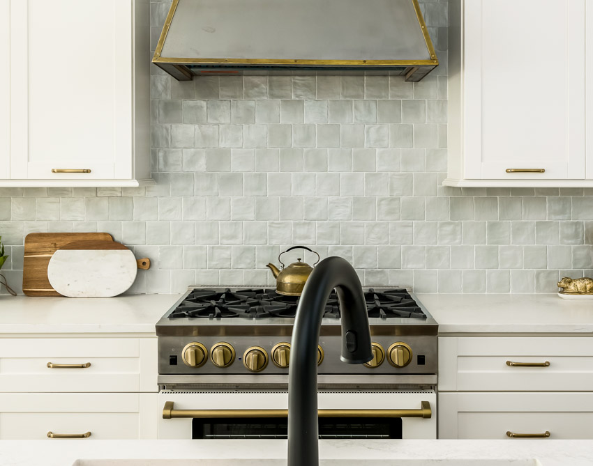 Kitchen with Mother of Pearl backsplash, range hood, countertop, cabinets, stove, and drawers