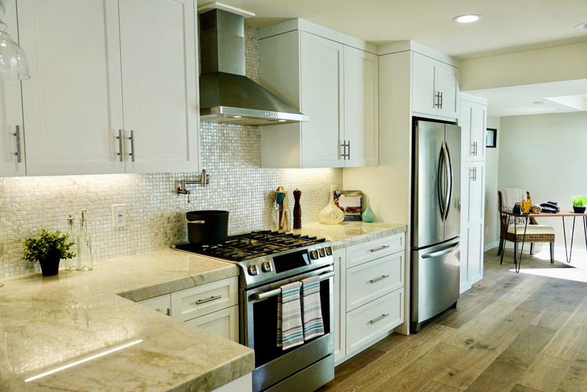 Kitchen with Mother of Pearl glass tile backsplash, countertops, cabinets, range hood, stove, and wood flooring