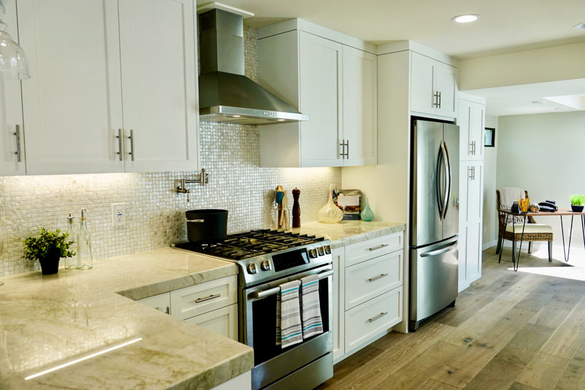 Kitchen with glass tile backsplash, white panel cabinets, range hood in chrome finish