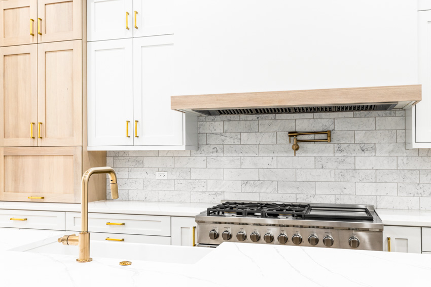 Kitchen with quartzite backsplash, tile cabinets, range hood, stove, and faucet