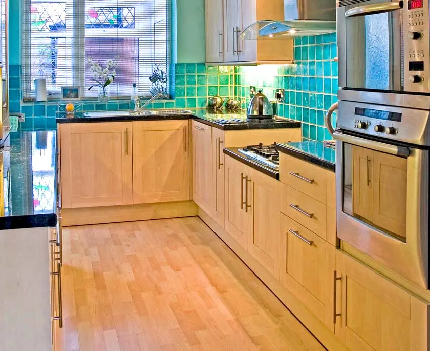 Kitchen with shaker maple cabinets, wood floor, tile backsplash, countertops, window, stove, and oven