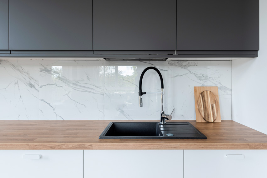 Kitchen with matte black sink, faucet, quartzite splashback, cabinets, and wood countertop