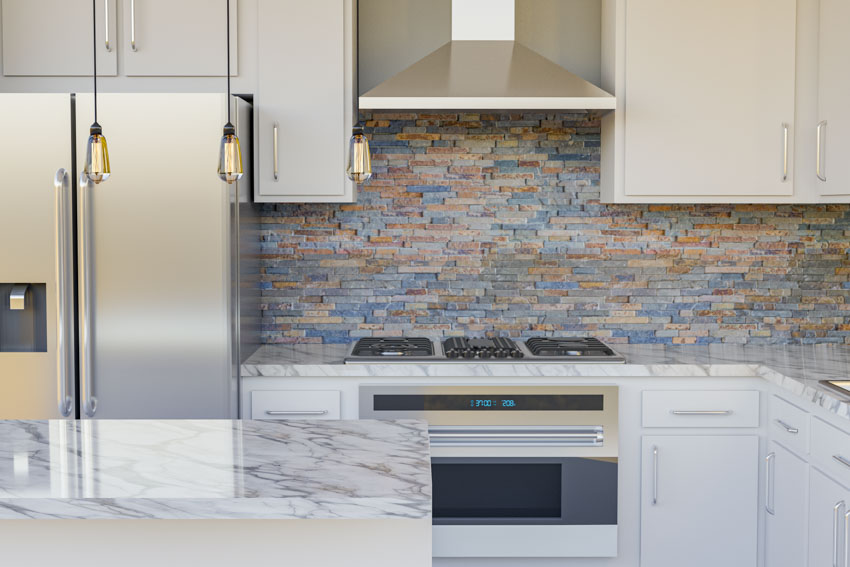 Kitchen with stacked stone backsplash, countertop, range hood, refrigerator, and cabinets