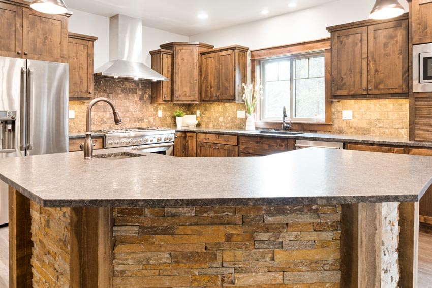 Kitchen with stone backsplash, countertops, island, wood cabinets, refrigerator, faucet, and windows