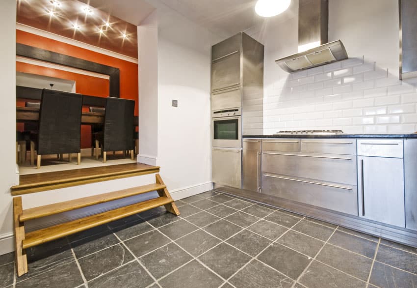 Kitchen with ceramic tiles, countertop, range hood, small wooden stairs and cabinets