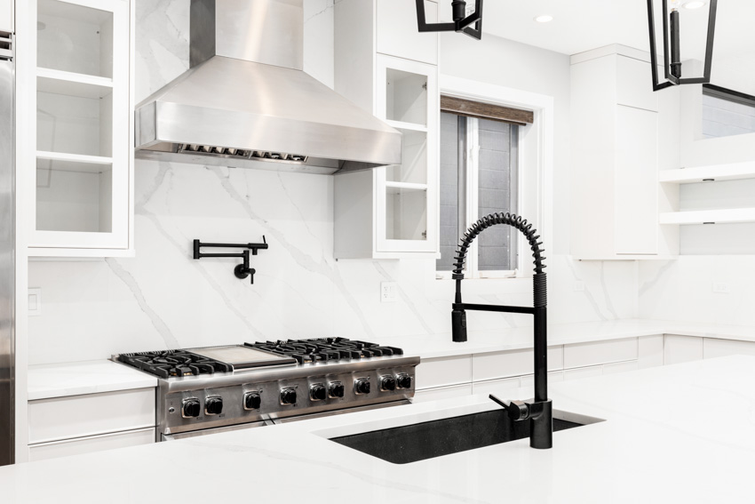 Kitchen with white countertops, stove, range hood, sink, faucet, and quartzite backsplash