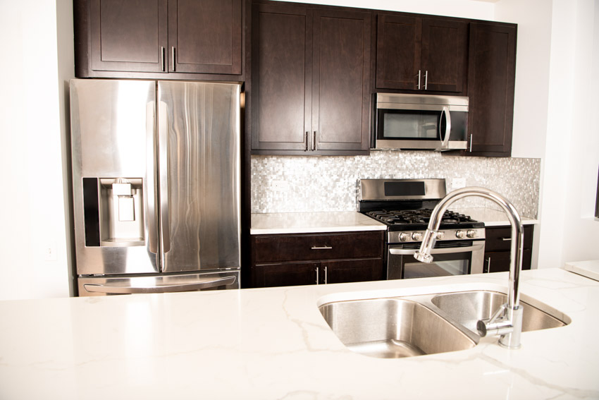 Kitchen with wood cabinets, refrigerator, countertop, sink, faucet, and Mother of Pearl backsplash