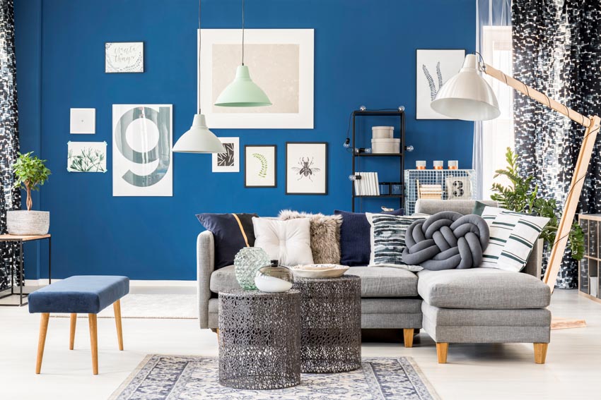 Living room with analogous pairing of gray furniture, sofa, coffee table, small ottoman, blue wall, floor lamp, and pendant light