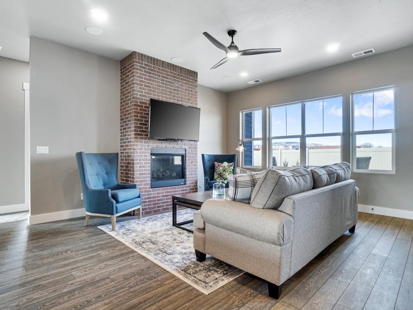 Living room with ceiling fan, cushioned sofa, chairs, fireplace, windows, and wood flooring