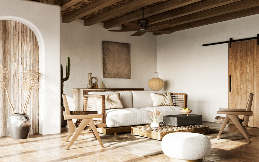 Living room with exposed ceiling beams, sofa chairs, barn style door, ottoman, and ceiling fan