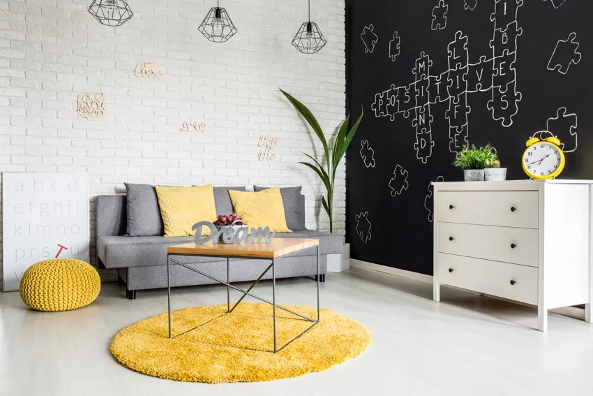 Room with chalkboard accent wall, white brick wall, console table and yellow rug