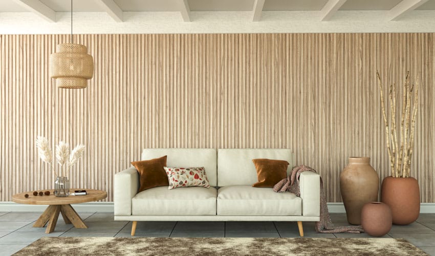 Living room with interior wood slat wall, sofa, side table, wood ceiling beams, jars, and rug