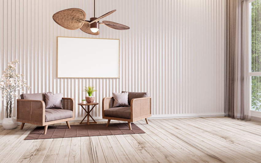 Living room with low profile ceiling fan, chairs, wood slat wall, side table, and wooden flooring
