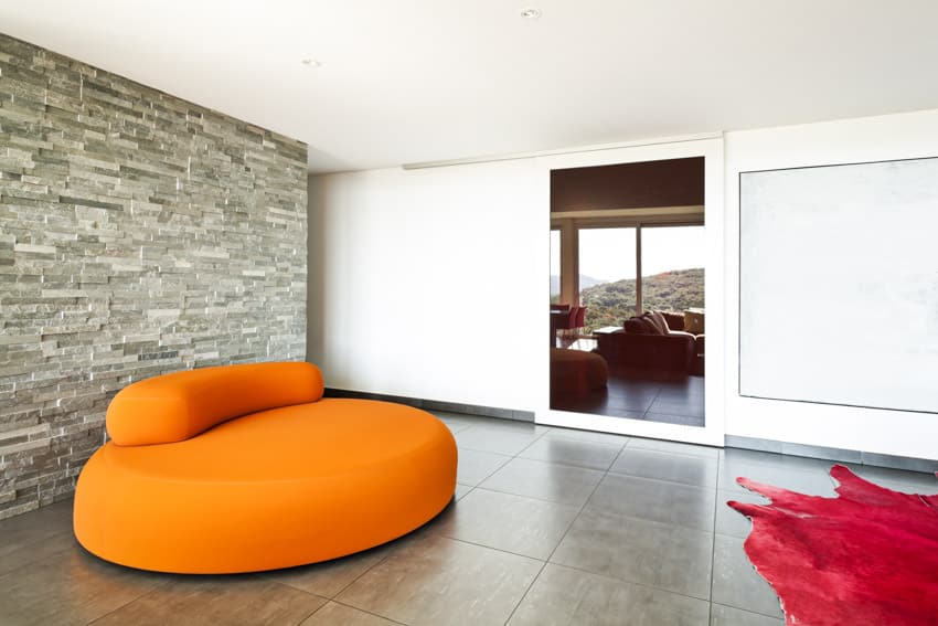 Living room with stone look vinyl flooring, orange cushioned chair, and accent wall