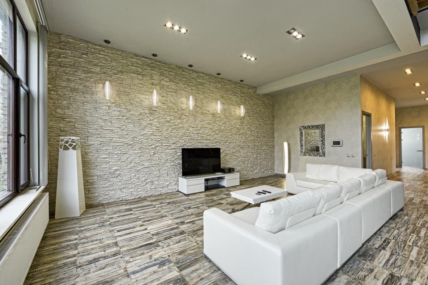 Living room with white sofa, television, TV stand, ceiling lights, and stone look floor tiles