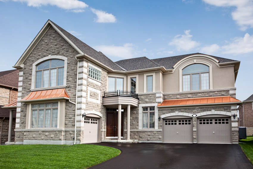 Luxurious house exterior with stone siding, garage, driveway, windows, and pitched roof