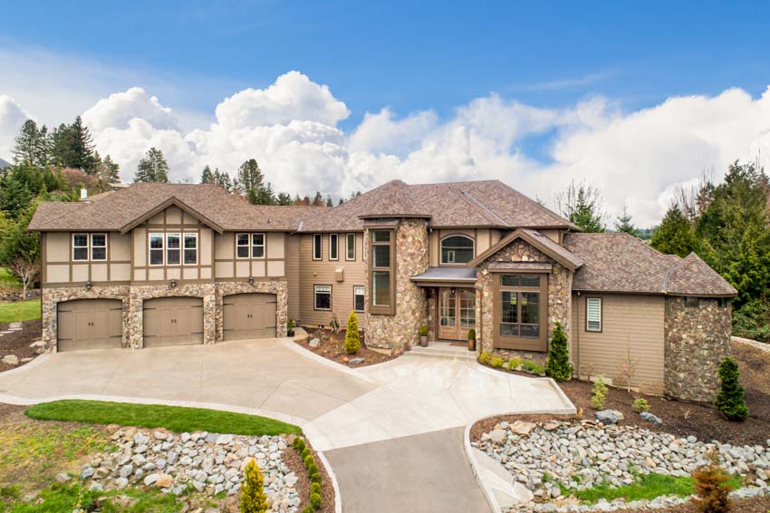 Luxurious mansion with exterior stone siding, garage, driveway, windows, lawn, and landscaping rocks