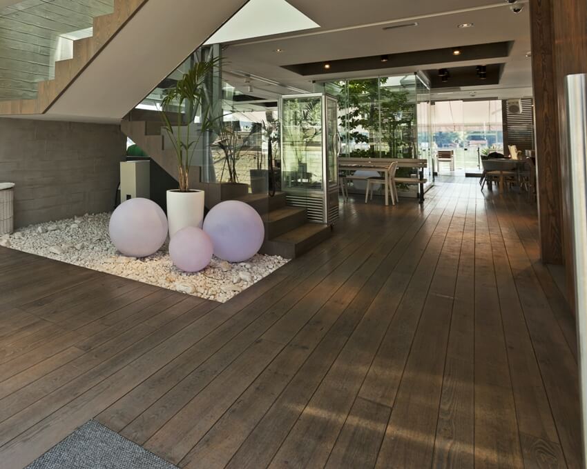 Luxury villa showing spacious alley near the stairs with floating engineered wood floors, pebble stones below the stairs with some pastel color decors and plants