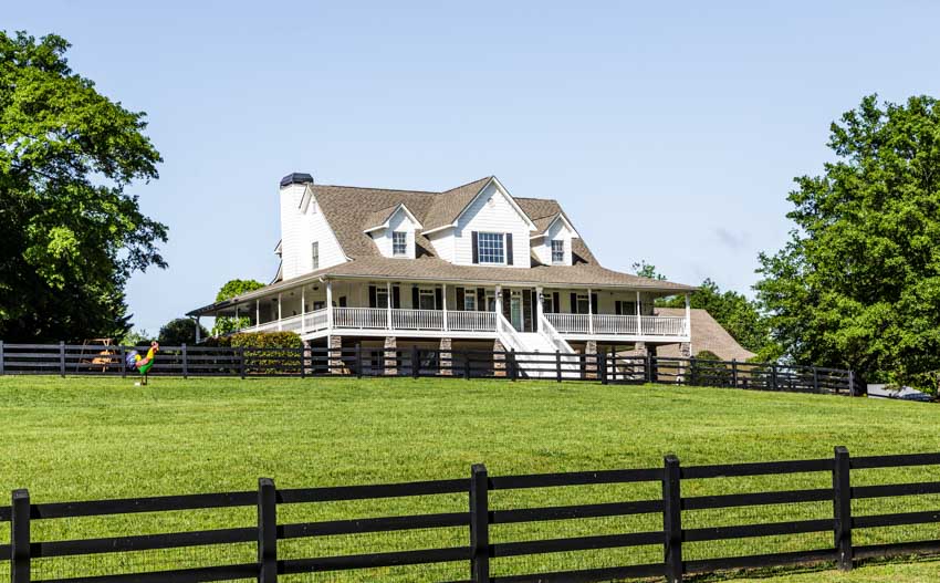 Mansion with dormer, front porch, grassy field, and metal split rail fence