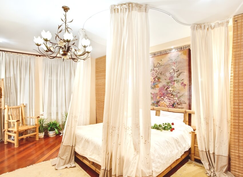Medieval style bedroom with ceiling mounted canopy bed, a chandelier, and a bamboo armchair on the side