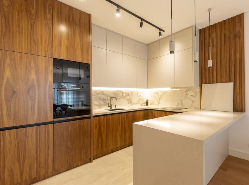 Modern kitchen with premium grade teak cabinets with built in oven, white countertops with marble backsplash and track lights