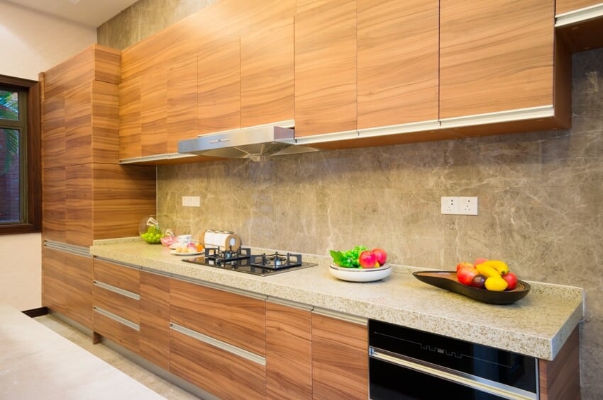Modern kitchen with skim coated walls, teak cabinet doors and granite countertop with some fruits and food on it and built in stove top
