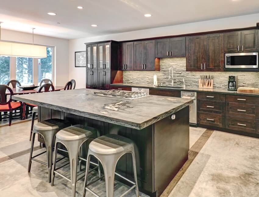 Kitchen in grey tones with dark wood storage, stone backsplash and center island 