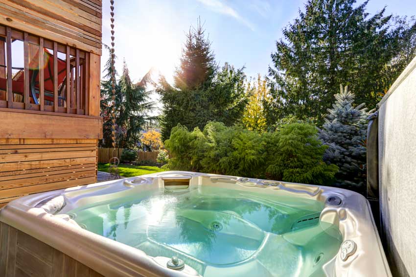 Outdoor area hot tub with hedge plants, fence, and wood siding