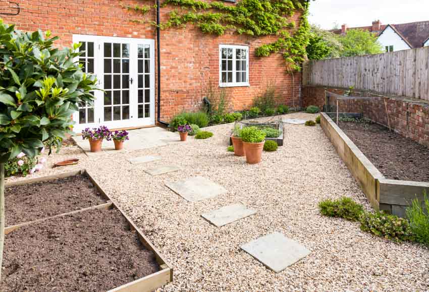 Outdoor area with gravel pavers, raised garden beds, brick wall, and window
