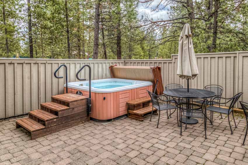 Outdoor area with hot tub, fences, table, chairs, and paved patio