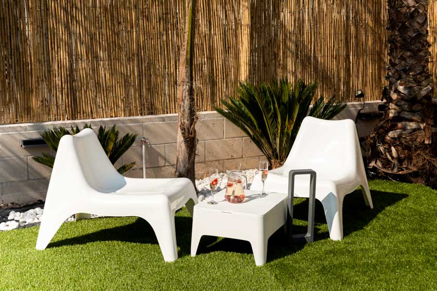 Outdoor area with white chairs and small table on grass wood fence and plants