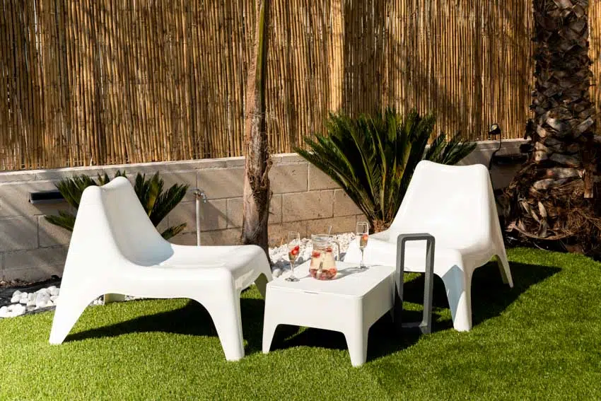 Outdoor lounge with white chairs, fake grass, small table, wood fence and plants