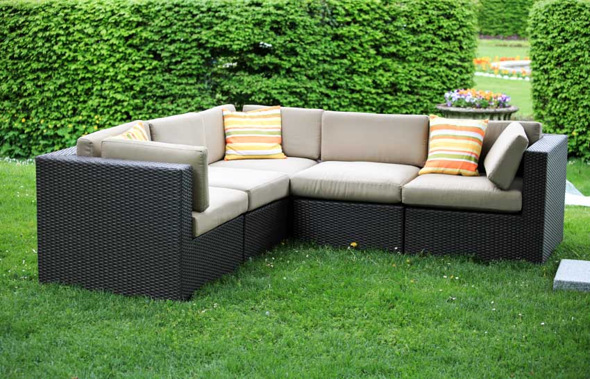 Outdoor cushioned sofa on grass with hedge plants behind it