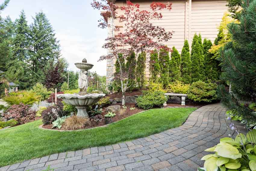 Outdoor garden with pavers, walkway, fountain, trees, and flowers