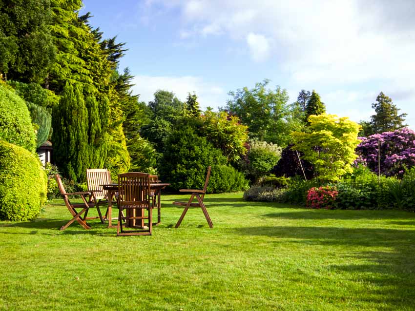 Outdoor grassy area with wood chairs, table, trees, and flowers