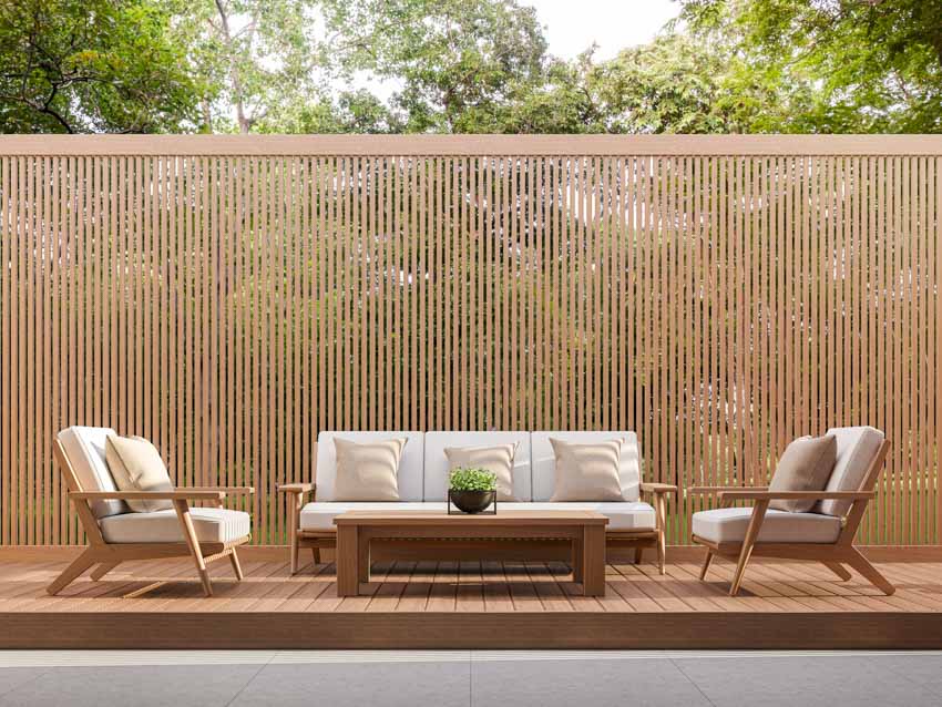 Outdoor living area with slat privacy wall, cushioned couch, chairs, and wood deck