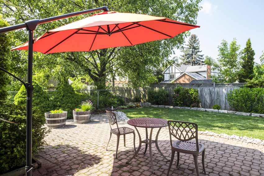 Outdoor patio with cantilever umbrella, shade, interlocking paver, table, chairs, trees, and fence