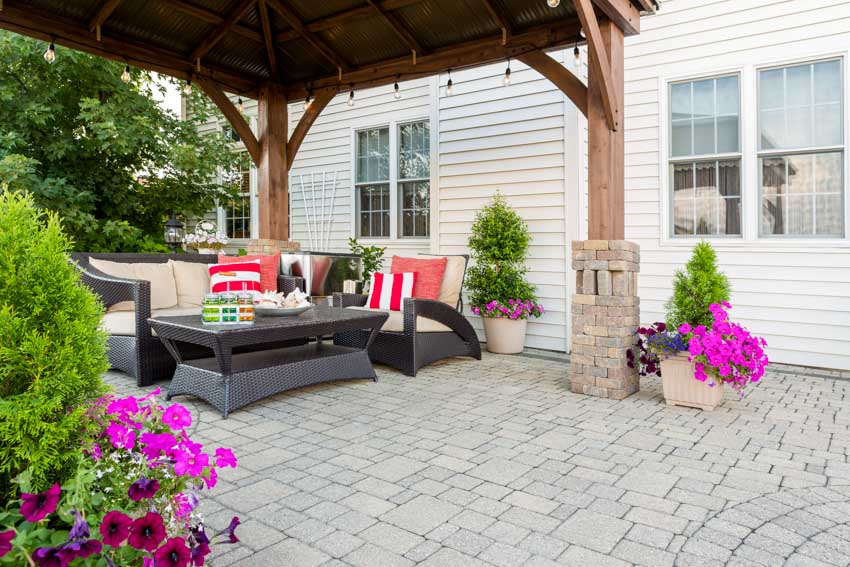 Outdoor patio with pavers, cushioned sofa chairs, coffee table, pergola plants, and trees