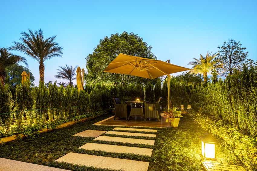 Outdoor patio with walkway, table, chairs, lighting fixtures, and cantilever umbrella