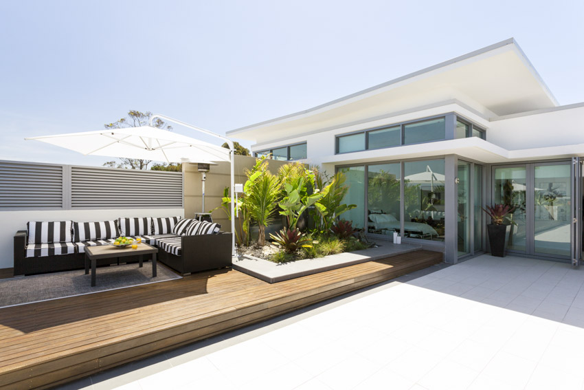 Outdoor patio with wood deck, cantilever umbrella, sofa, fence, table, and plants