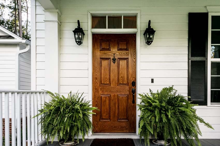 Outdoor porch with front wooden door, siding, and wall sconces