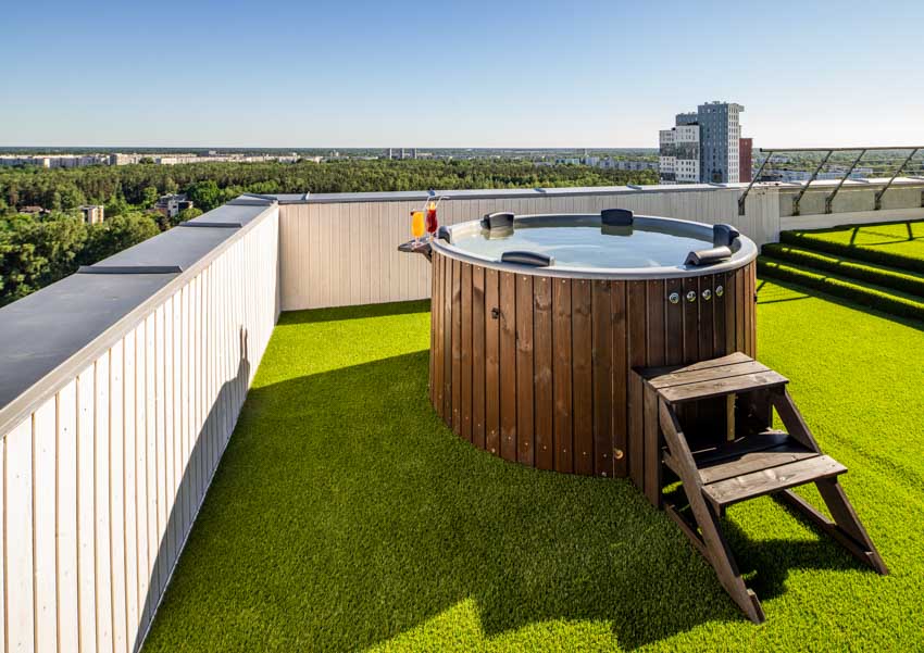 Outdoor roof area with wood hot tub, fake grass, and privacy fence