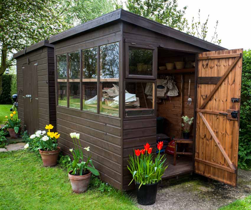 Outdoor shed with wood plank siding, windows, door, and potted flowers around it